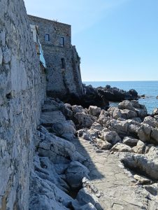 Stone pathway around a stone wall and castle right next to the sea.