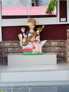 Goddess Saraswati statue holding a veena, dressed in a white and pink sari, with a swan beside her.