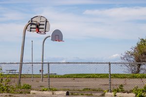 Basketball hoops on an old cement court behind a chain link fence.
