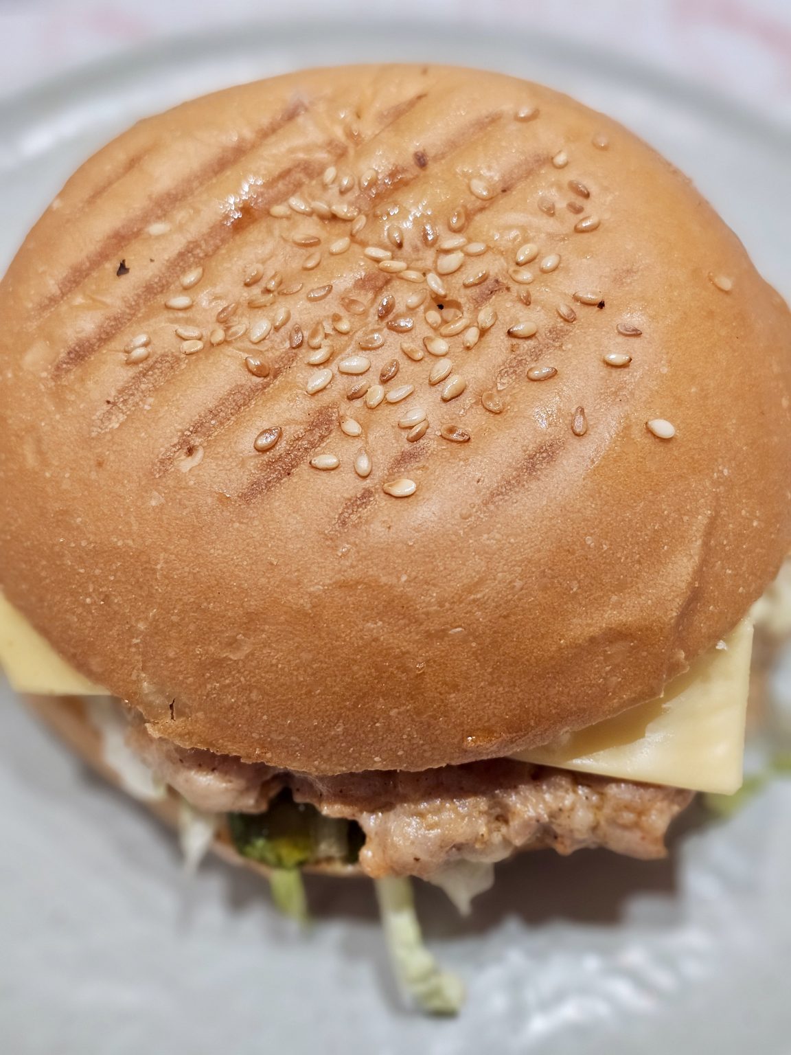 A close-up photograph of a juicy burger with a golden sesame-seed bun, melted cheese, and a visible meat patty. The warm tones and detailed bun texture make the food look appetizing. Location: Kozhikode, Kerala.