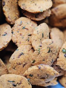 A detailed close-up of a stack of crispy golden-brown savory snacks (Parippu vada, also known as masala vada or dal vada), with pieces of onion and green herbs visible on the surface. The tight composition highlights their texture, color, and freshly fried appearance. Location: Sanketham Viewpoint, Kozhikode, Kerala.