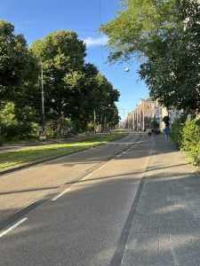A cobblestone path bordered by grass leading to a large stone arch with classical architecture.