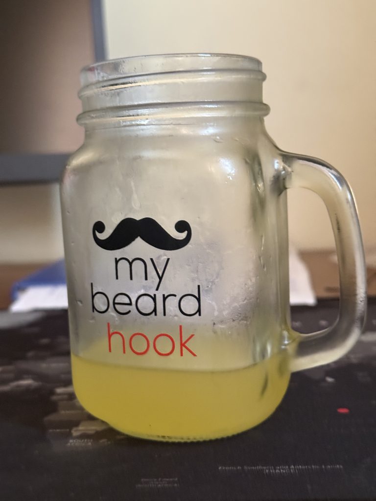 A chilled glass cup with yellow passion juice and the words "My Beard Hook"