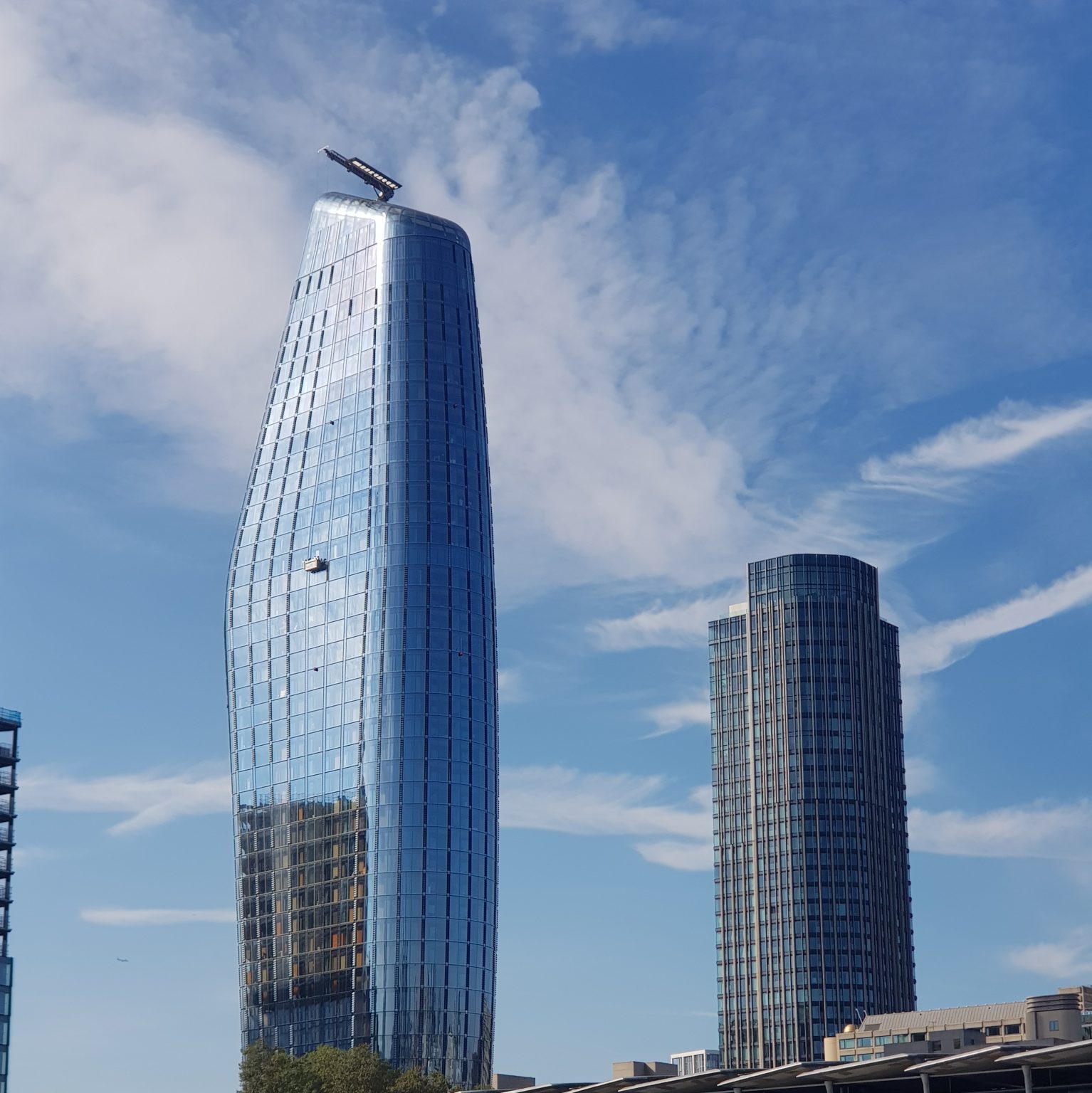Curving glass towers reflecting blue sky beside a shorter cylindrical building.