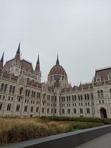 Intricate Neo-Gothic facade and central dome of the Hungarian Parliament Building in Budapest viewed from ground level under an overcast sky.