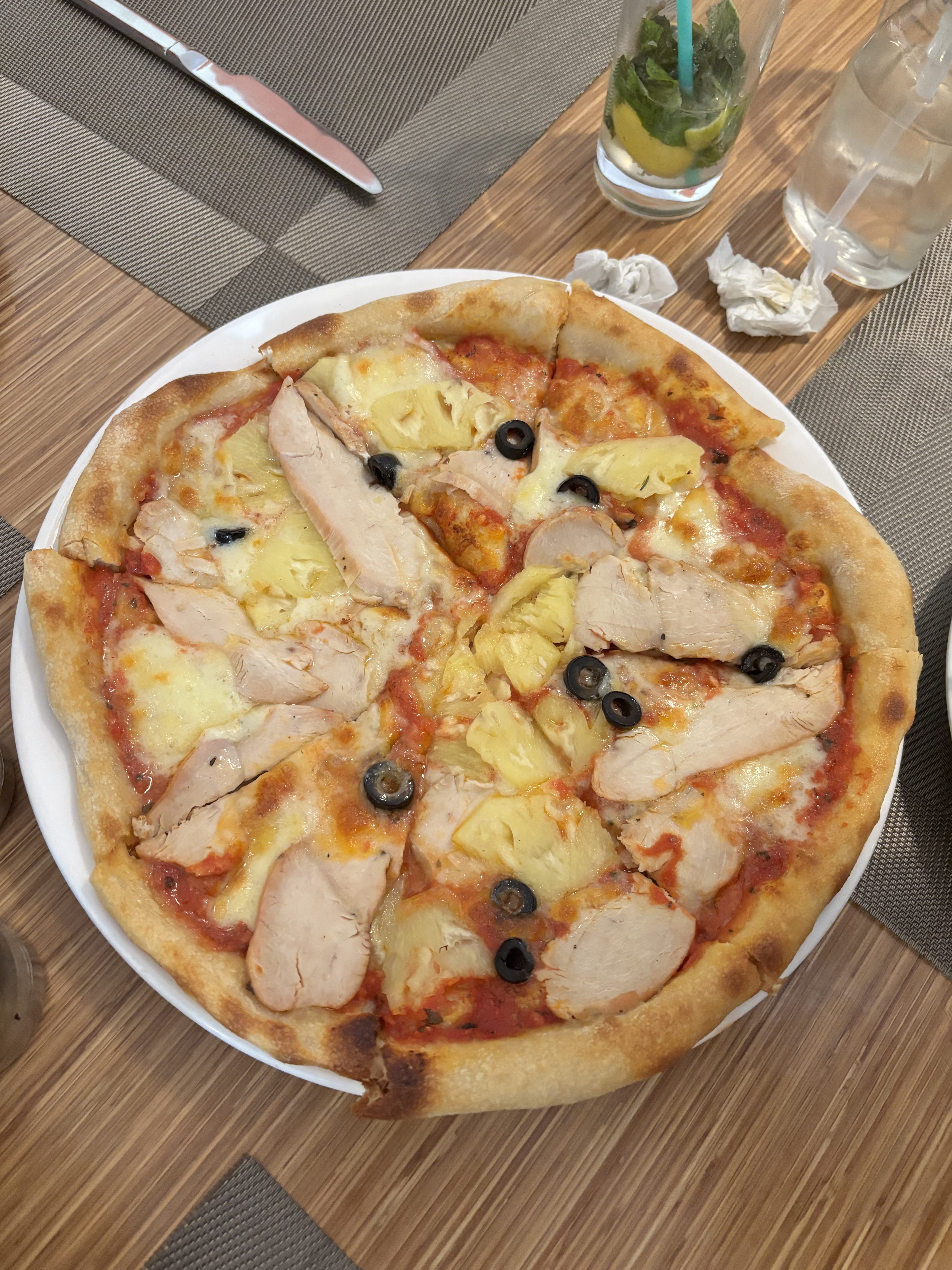A round pizza is sitting on a white plate. The crust is golden brown and slightly charred at the edges.