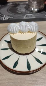 Lemon Mousse Cake topped with three white piped meringue swirls, served on a decorative white plate with green leaf patterns.