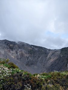 
A panoramic view of a volcanic crater, featuring steep, rocky walls that rise sharply against a cloudy sky.