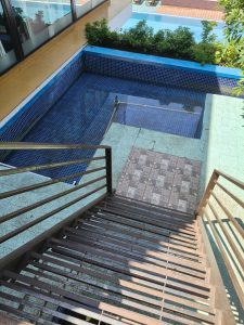 
A set of metal stairs leads down to a small, rectangular pool area, which is surrounded by blue-tiled walls