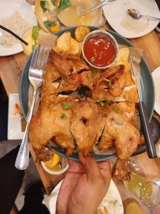 A platter of whole golden fried chicken cut into quarters and served with crispy potato chips and a side of red dipping sauce.