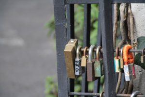 Close-up of several love padlocks in different colors, sizes, and metals attached to a black wrought iron fence railing.