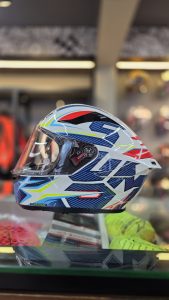 A full-face motorcycle helmet with an aerodynamic shell, displayed on a glass shelf in a store.