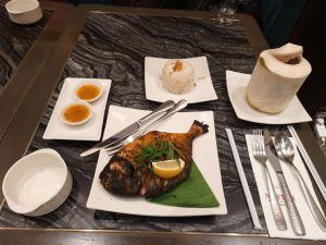 Grilled fish with scallions and lemon, served with garlic rice, dipping sauces, and a fresh coconut drink on a banana leaf.
