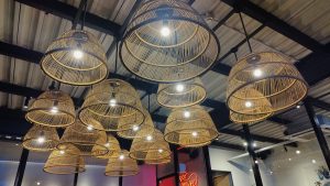 Several tiered woven bamboo pendant lights hanging from a dark, exposed ceiling in a modern restaurant or cafe.
