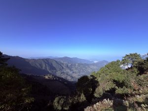 A high-elevation panoramic view overlooking deep forested valleys and rolling green mountain ranges stretching toward the horizon under a clear sky.
