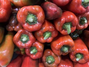 
A pile of red bell peppers with glossy skin and green stems.