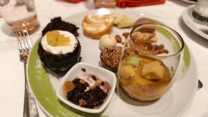 An assortment of sweet desserts including a chocolate cup, mini cream rolls, sesame balls, dried fruits, and mango mousse in a glass.
