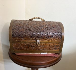 A vintage style, hand carved wooden dome topped keepsake box featuring intricate floral leaf motifs and an antique brass finish clasp.