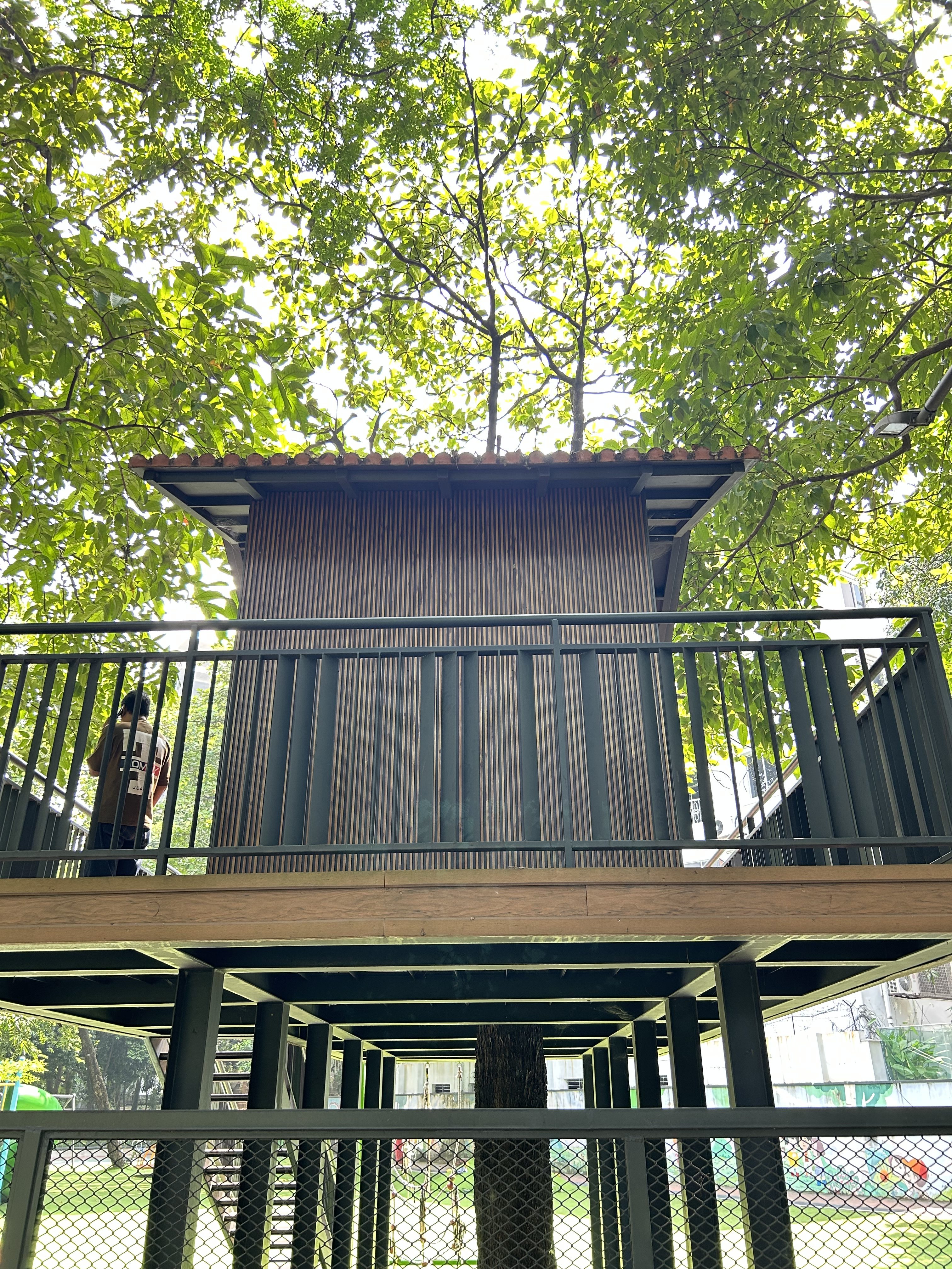 A raised wooden structure with an orange tiled roof, balcony, and a tree growing through its base.