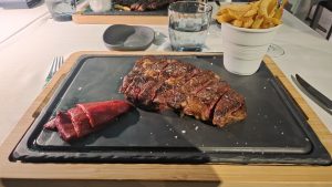 Grilled beef steak on a dark slate board with French fries and sliced red pepper on the side.