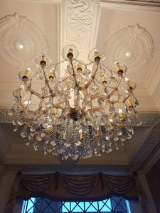 A multi-tiered crystal chandelier with sparkling glass pendants hanging from an ornate white molded plaster ceiling.