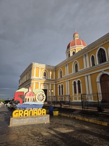 Granada Cathedral with a red dome and a colorful Granada sign on a wet stone pavement.
