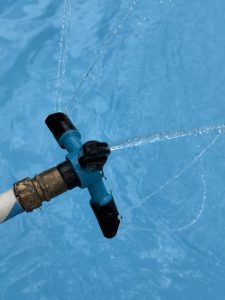 Rotating lawn sprinkler spraying water in arcs into a kids pool

