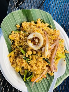 Spicy squid fried rice with vegetables served on a banana leaf, with a white plastic spoon beside it.