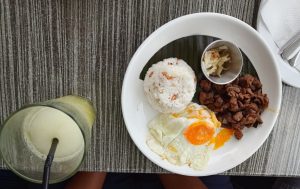 Filipino breakfast with garlic fried rice, a fried egg, beef tapa, pickled papaya, and an iced calamansi drink.