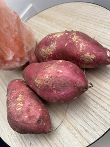 
Three reddish-purple sweet potatoes with textured skins and thin roots resting on a round wooden surface.