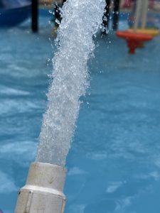 Water jet spraying into a swimming pool with children play material blurred in the background