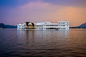 Udaipur Cityscape: A panoramic view of Udaipur showing historic buildings, palaces, greenery and Lake Pichola, with the surrounding Aravalli hills forming the backdrop.