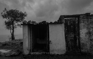
A small, weathered structure stands against a cloudy sky, with a tree nearby. 