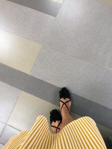 Top-down view of someone wearing a yellow-and-white striped dress and black floral flat sandals, standing on a tiled floor. #wcsylhet2026