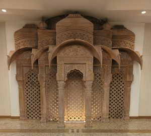Intricate Rajasthani carved architectural panel with symmetrical arches, lattice screens, floral motifs, and decorative columns.