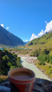 The river is flanked by steep, green-covered mountain slopes and rugged terrain, with a small cluster of buildings or a village nestled in the valley floor.