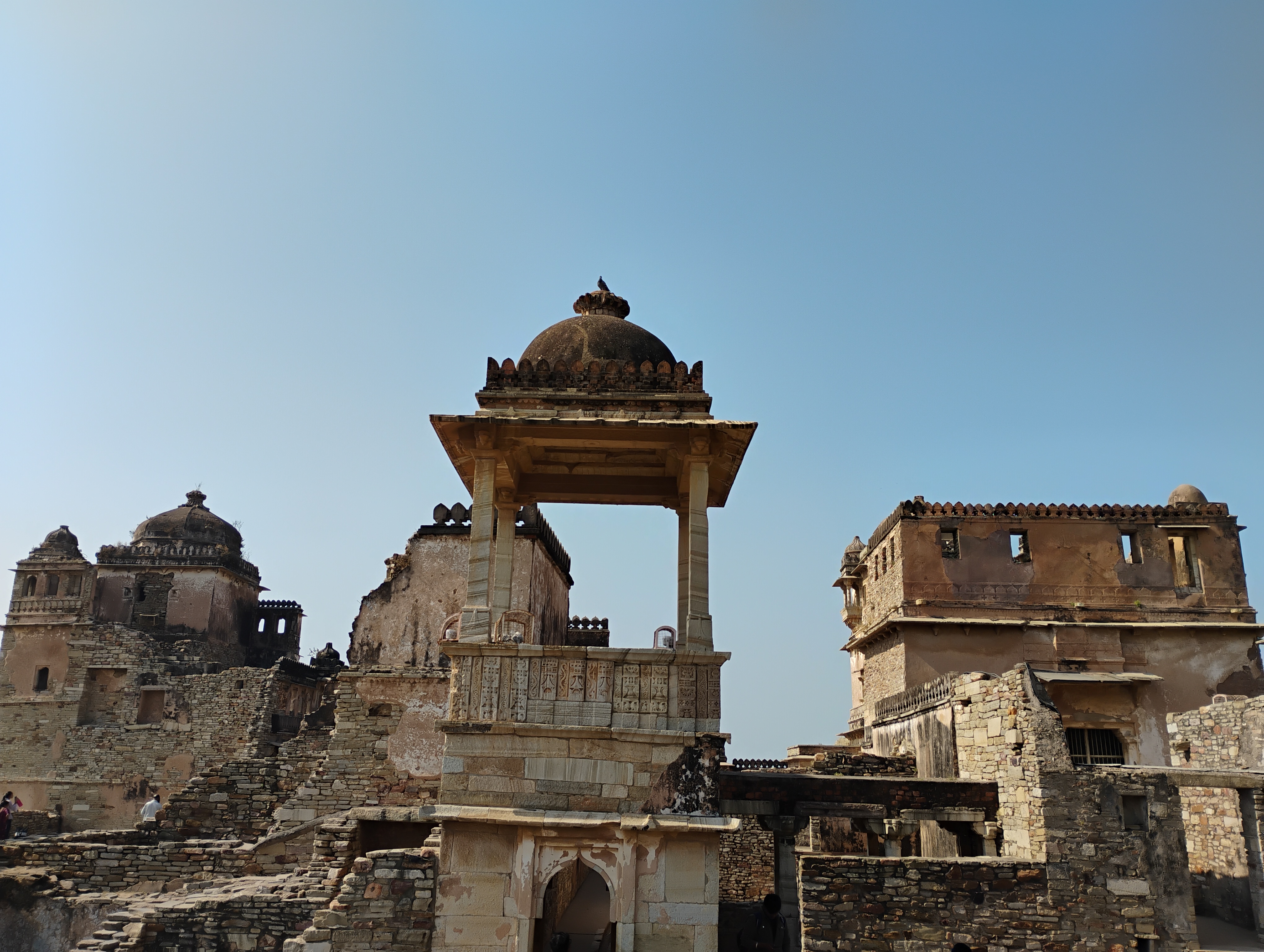 An ancient stone monument complex with domed structures and weathered architecture under a clear blue sky.