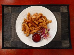 A plate of seasoned potato fries garnished with chopped herbs, served with a side of coleslaw salad and tomato ketchup in a small dipping cup.