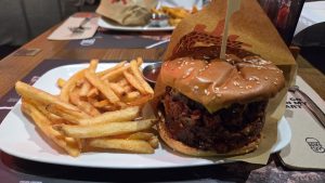 A gourmet burger and french fries are served on a white plate on a wooden table.