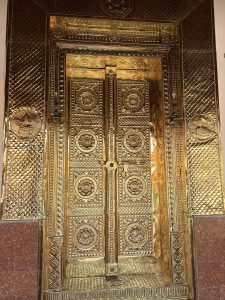 Ornate gold-plated temple door with floral designs, geometric panels, and traditional pot-shaped decorations.