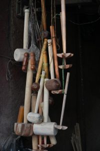 A collection of wooden mallets for cooking, as well as some other tools, all hanging vertically as if in storage in a kitchen.
