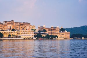 Lake Palace, Udaipur: The white Lake Palace stands serenely in Lake Pichola, surrounded by calm water and silhouetted hills beneath a soft evening sky.