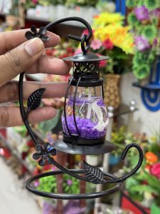 Close-up shot of a decorative metal lantern holder being held in a hand, featuring a black stand with decorative leaves and flowers