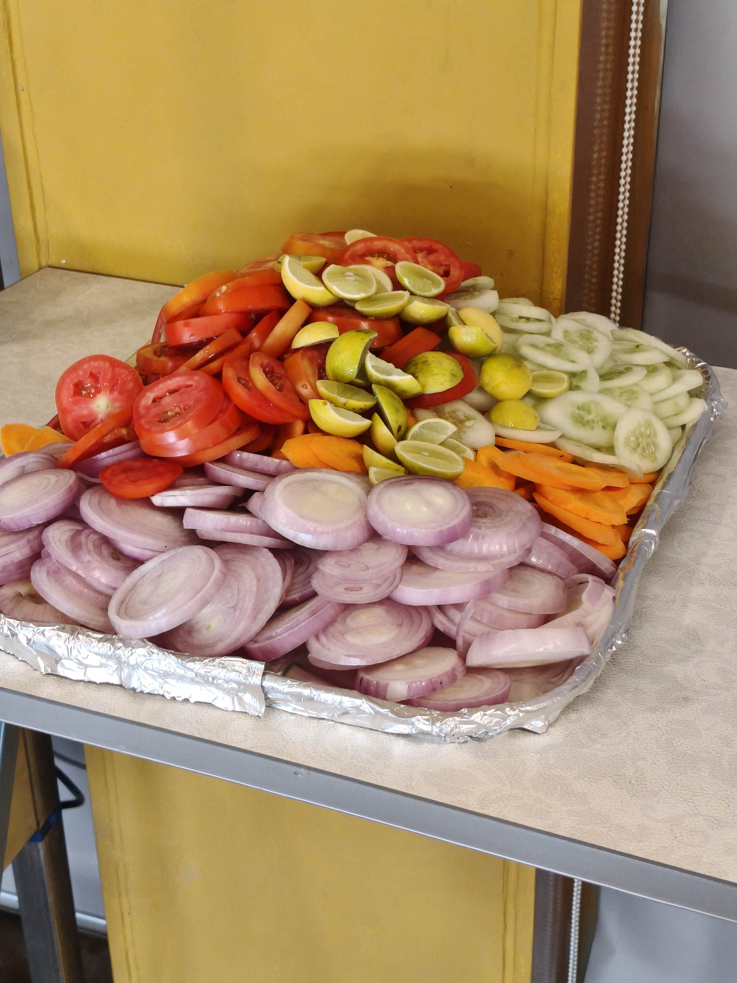 Sliced tomatoes, cucumbers, carrots, red onions, and lemons arranged on a foil-lined serving tray.