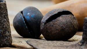 Close-up macro shot of two rusty, spherical metal bells with a split opening, resting on a textured wooden surface among other metallic artifacts.