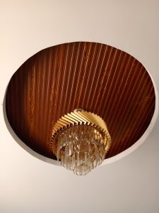 A tiered crystal chandelier hanging from a circular wood-paneled ceiling alcove surrounded by a smooth white ceiling.