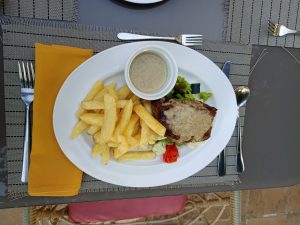 
Grilled steak with creamy peppercorn sauce, thick-cut fries, steamed vegetables, and a side of extra sauce on a white platter.