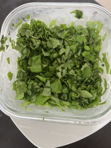 A clear glass container filled with finely chopped green spinach. The leaves are vibrant and fresh, showing various shades of green with a slightly glossy appearance from moisture.