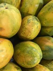 Several yellow and green papayas piled together, with spotted and speckled skin.