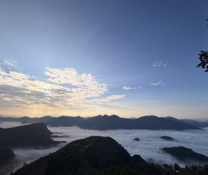 The breathtaking view from the top of the hill with hill ranges and clouds beneath them with the clear weather and rays of sunlight